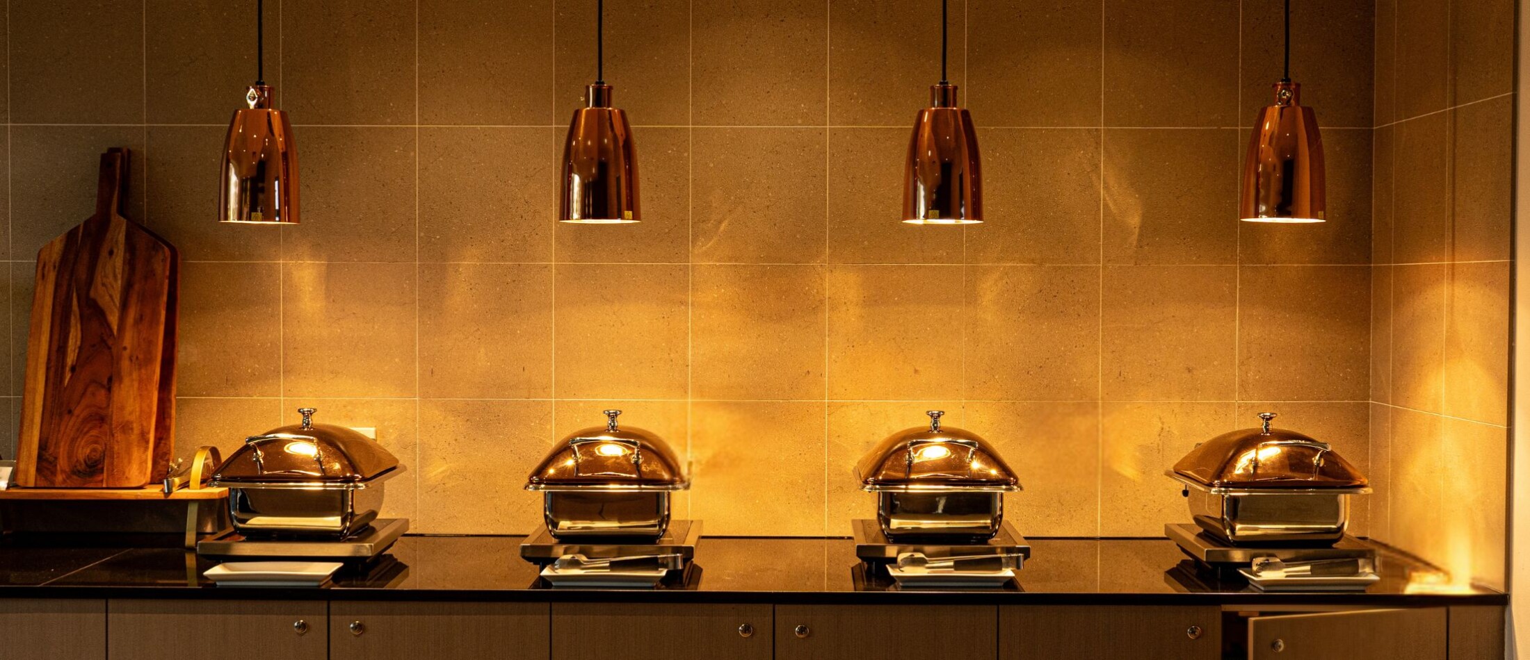 Buffet counter with chafing dishes under two copper pendant lights at Comfort Resort Leura Gardens.