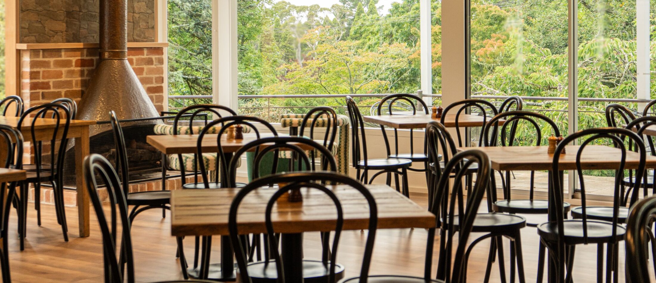 Fairways Restaurant & Bar at Comfort Resort Leura Gardens with wooden tables, dark chairs, and large windows facing lush greenery.