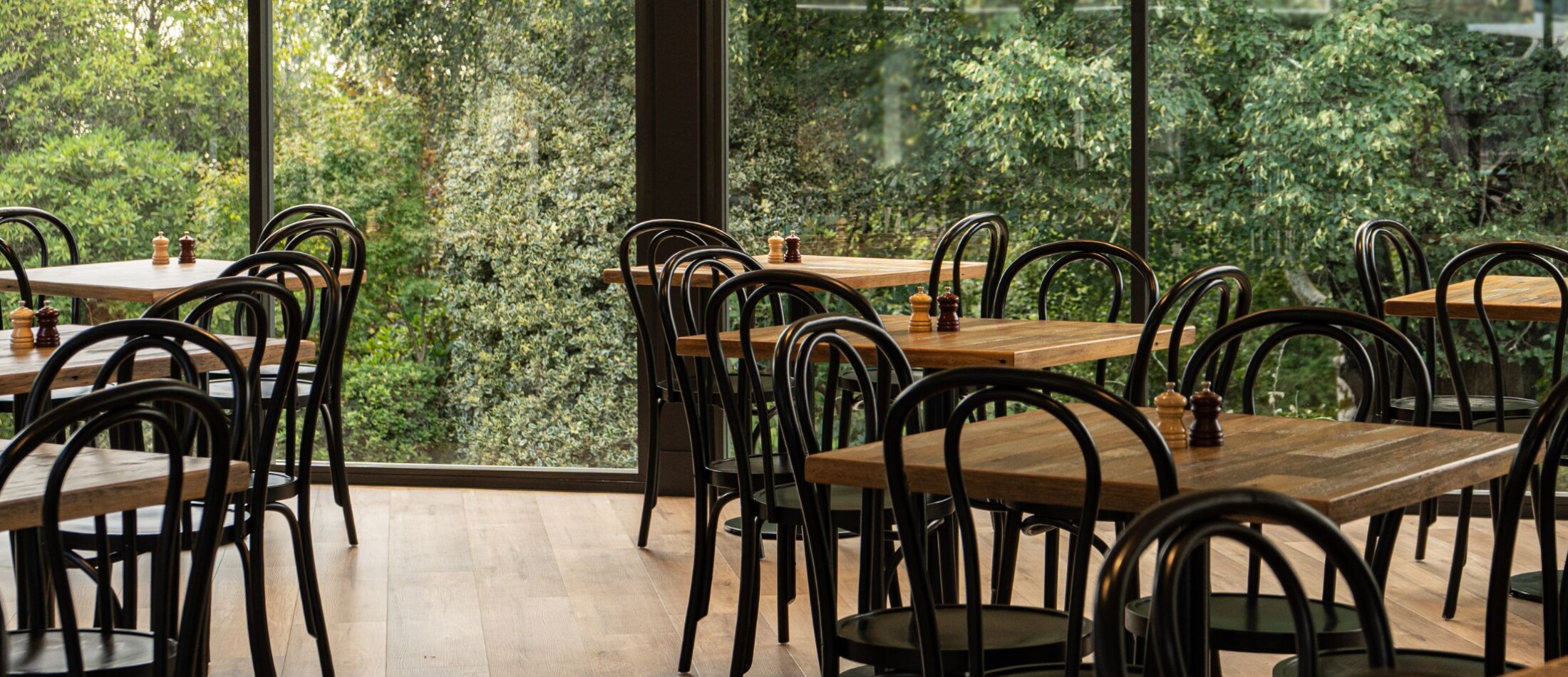 Dining room at Comfort Resort Leura Gardens with wooden tables, dark chairs, and large windows facing lush greenery.